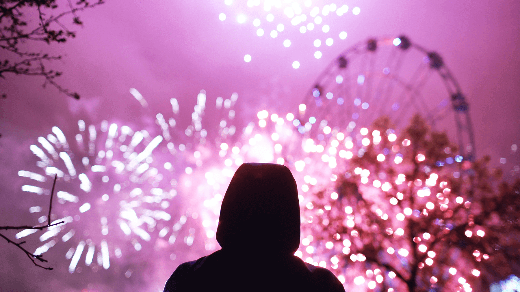 Man standing alone silhouetted against nighttime sky with fireworks.